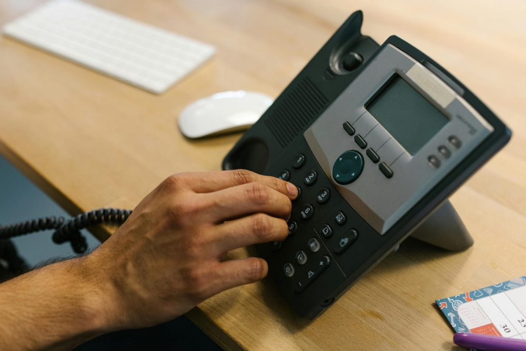 Une main compose un numéro de téléphone sur un bureau en bois. Environnement de bureau avec clavier et agenda.