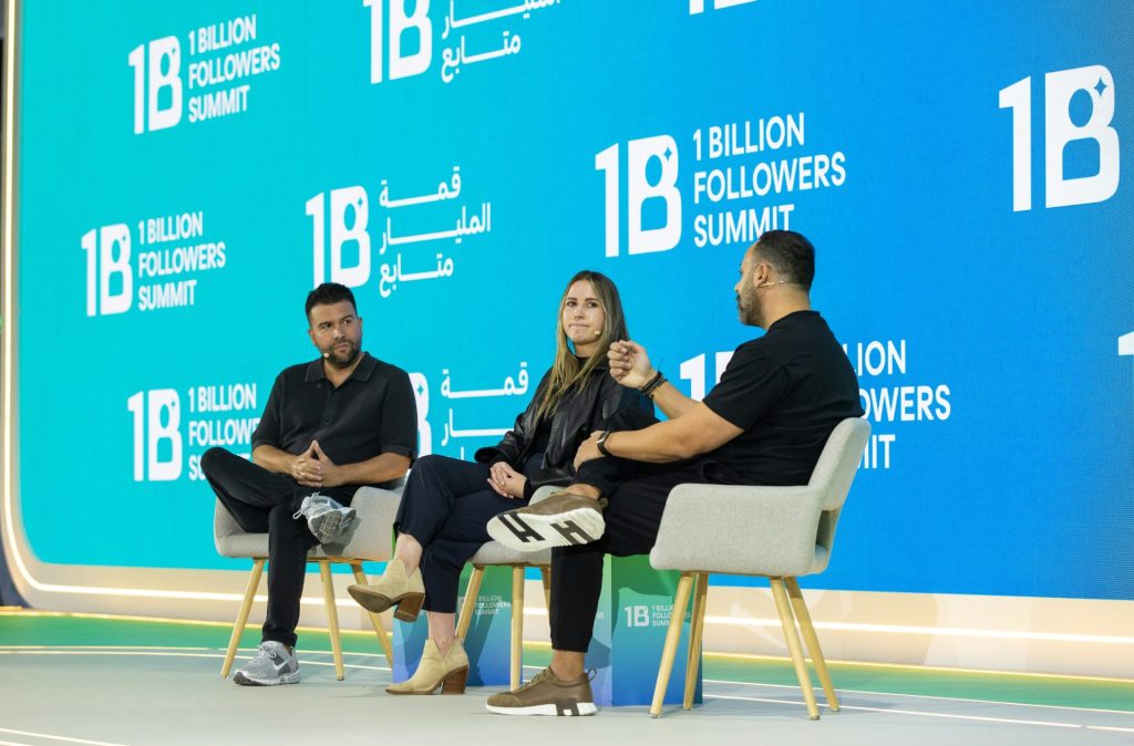 Three people sit on chairs on a stage discussing.