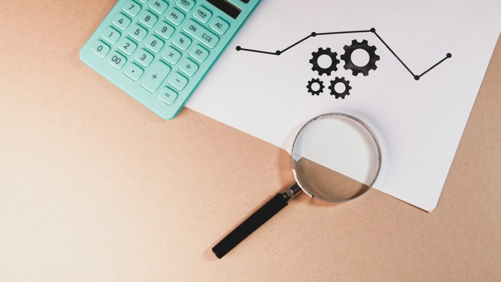 Calculator, magnifying glass, and chart with gears on paper.