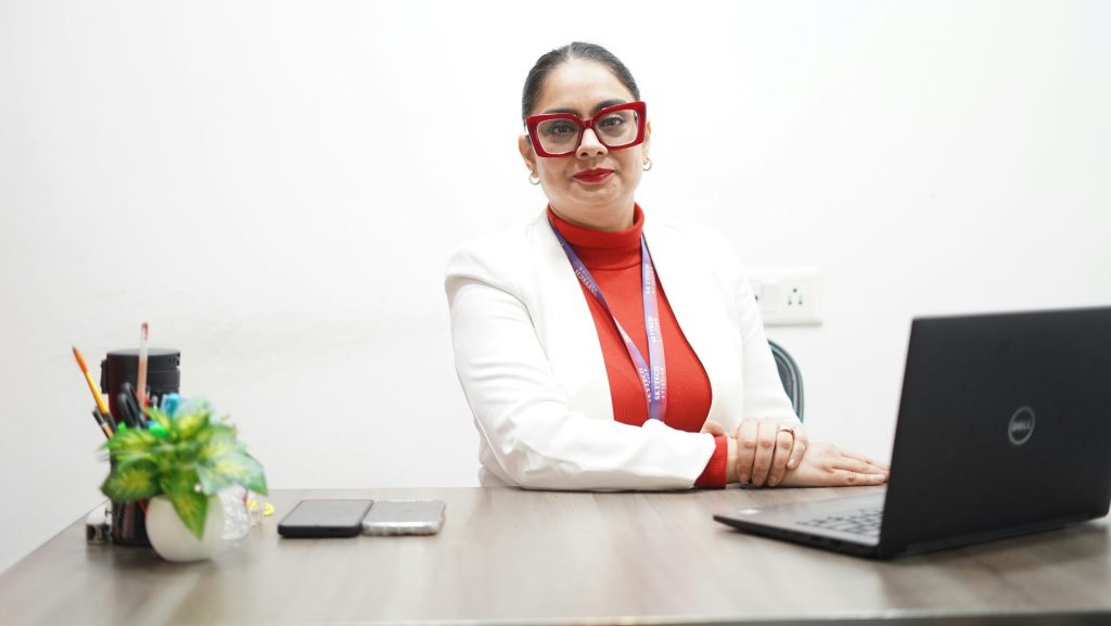 A woman in a white blazer sits at a desk.